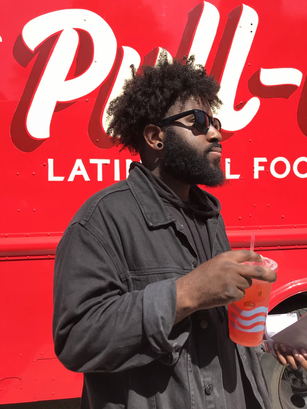 Man in sunglasses holding a drink in front of a bright red food truck